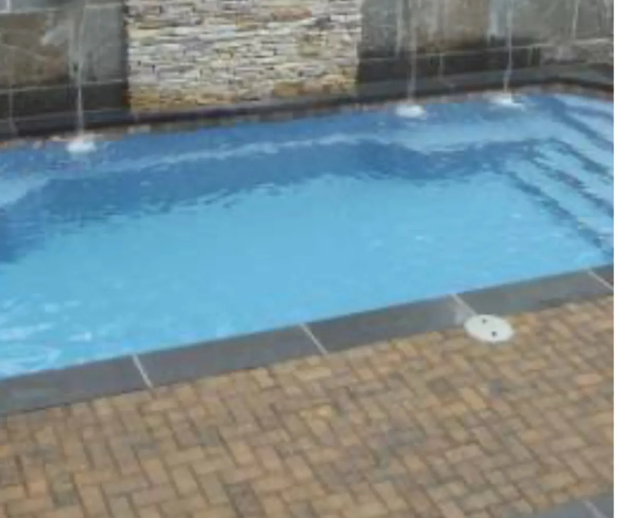 A stylish inground swimming pool set amid a stone patio, accentuated by water features and framed by a stone wall. The inviting space suggests social gatherings, sunbathing, and poolside relaxation.