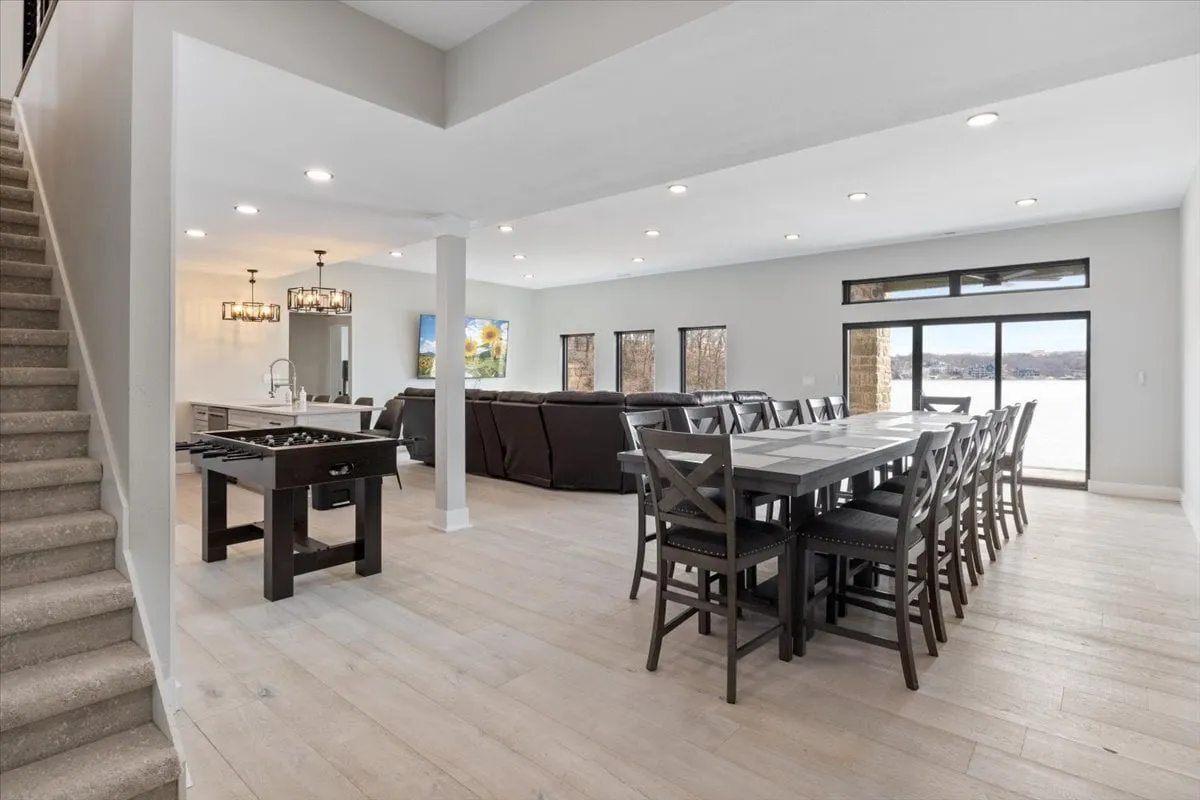 A large dining area with a spacious table for group meals, comfortable seating, a staircase leading to an upper level, and generous windows offering beautiful lake views. The room seamlessly connects with the social and culinary spaces, embodying an atmosphere of togetherness.
