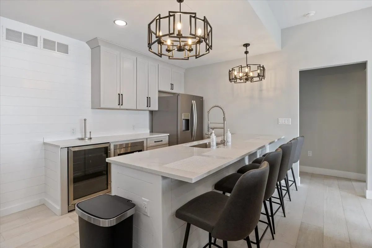 This image captures a modern kitchenette area with a spacious island countertop, chandeliers, and stainless steel appliances. The setting is contemporary and inviting—perfect for preparing snacks or drinks during game nights or wellness sessions.