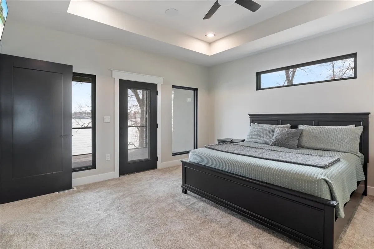A tranquil bedroom featuring a cozy bed positioned under large windows, allowing plenty of natural light to filter in. The room is accented with soft carpeting and simple furnishings, creating an inviting, peaceful atmosphere.