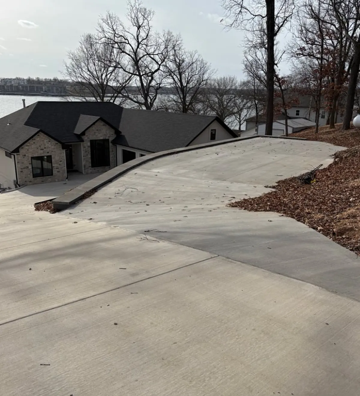 This image presents a striking exterior view of Grand Gaze, showcasing its modern architectural design surrounded by natural tree lines and overlooking the tranquil lake. The spacious yard and direct sightlines to the water emphasize the property's connection to its peaceful setting, suggesting ample outdoor space for group activities.