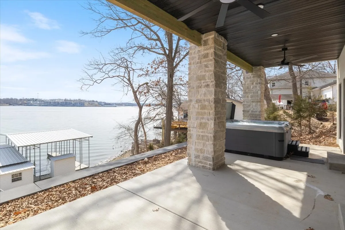 A serene view of a hot tub tucked among stone columns and trees, with a sweeping water view in the background. The setting is private and tranquil, ideal for relaxation while enjoying the lakeside atmosphere.