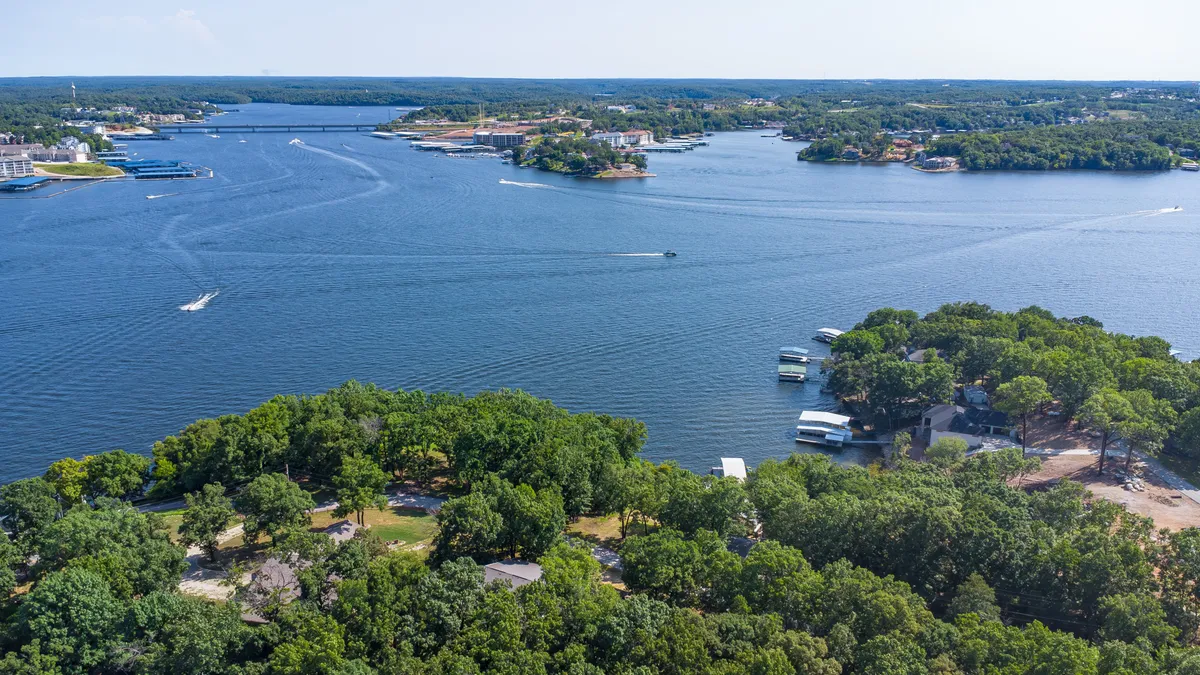 A sweeping view across the lake, featuring calm water, boating activity, and tree-lined shores. The scene is tranquil yet filled with the subtle excitement of water adventures, offering a perspective of the broader Lake of the Ozarks experience.