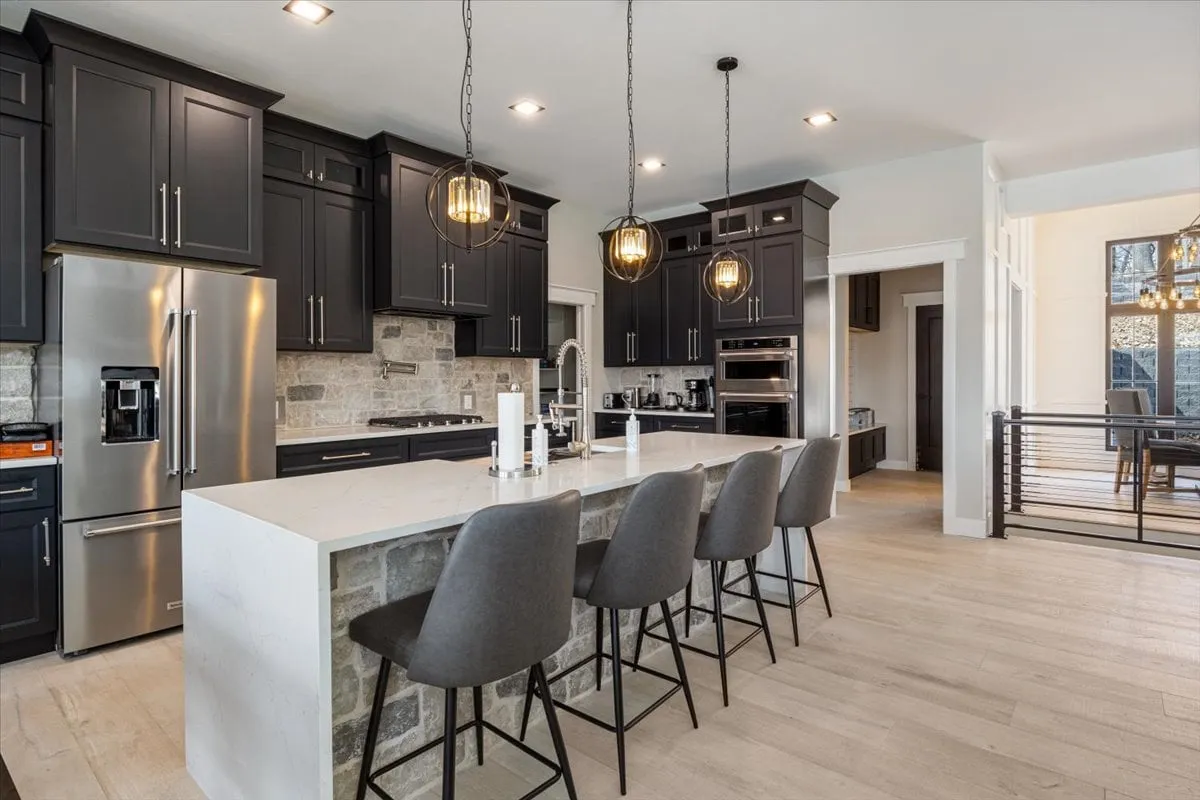 A modern, open-concept kitchen with a prominent island, sleek appliances, pendant lights, and a striking stone backsplash. The layout invites both cooking and socializing, making it ideal for preparing group meals or casual breakfasts.