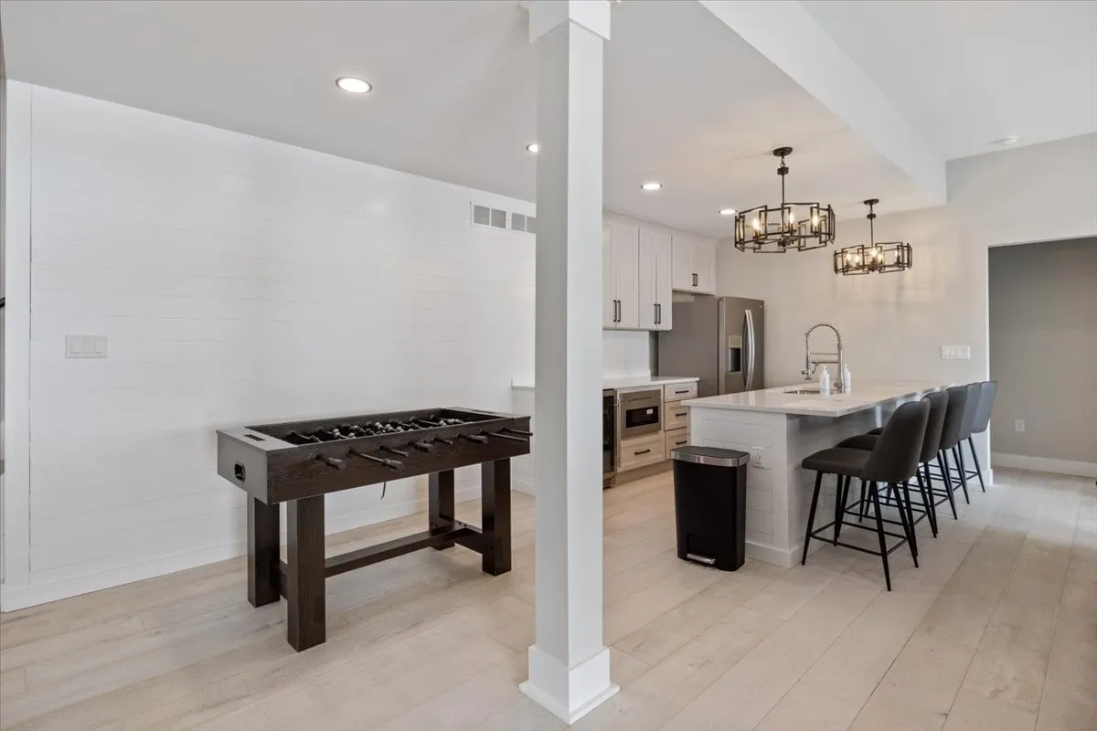 This image provides another view of the entertainment area, with the foosball table prominently featured alongside an island countertop, chandeliers, and bar stools. The casual, playful mood is enhanced by the open, social-friendly layout, ideal for game nights and gatherings.