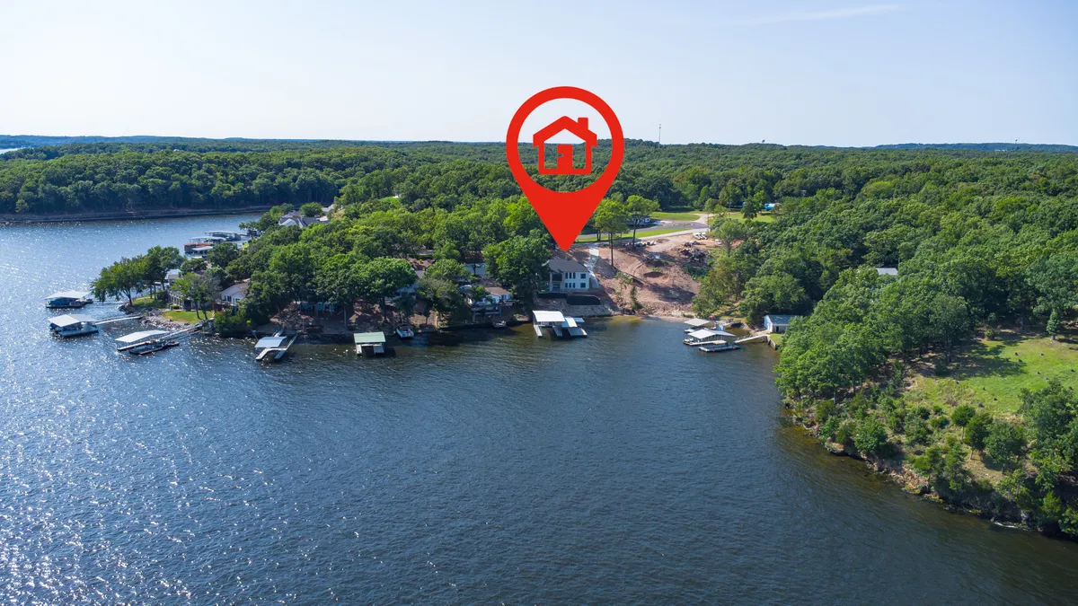 A stunning exterior shot featuring the lakefront, a private dock with boats, and lush greenery surrounding the water. The scene captures the essence of effortless lake access, water sports, and a tranquil lakeside atmosphere.