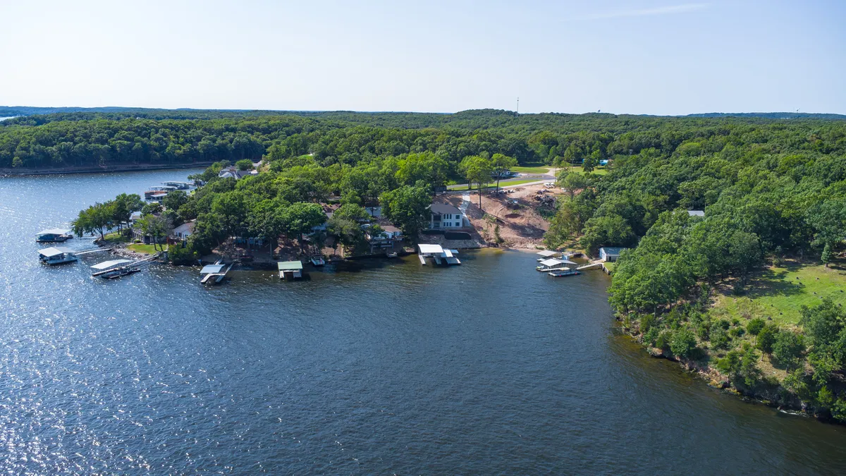 An inviting exterior view of the lakeside property, showcasing the expansive lake, multiple docks including private slips, lush surrounding greenery, and neighboring houses. The scene captures the essence of lakeside living with space for dockside activities and easy access to the water.