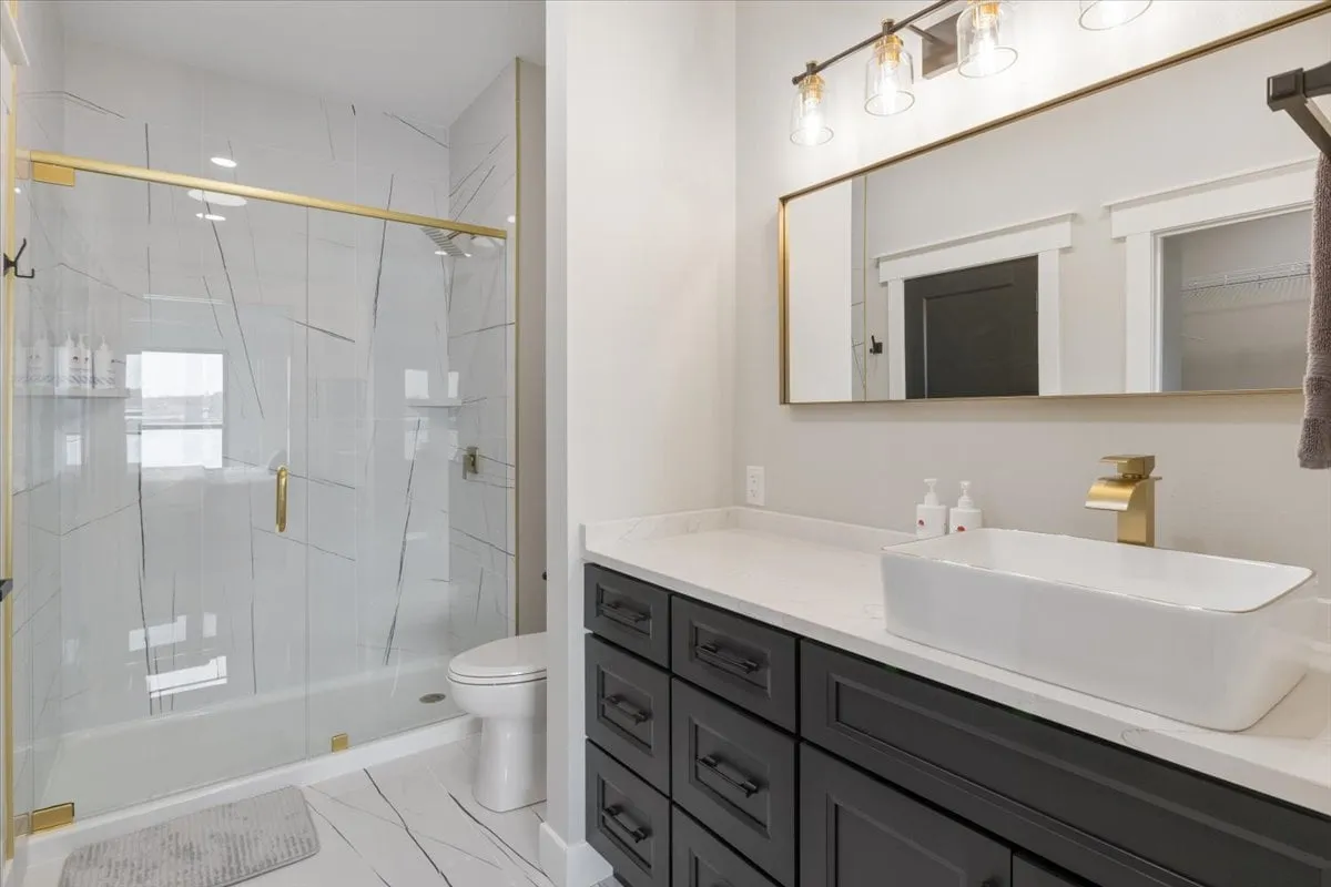 A calming bathroom scene with a glass-door shower, floating vanity, vessel sink, mirrored cabinet, and gold fixtures. The design radiates luxury and comfort, providing an ideal setting for rejuvenation and self-care.