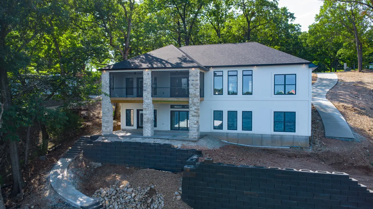 A welcoming front porch framed by large windows and surrounded by mature trees, with a stone facade lending a sense of exclusivity and comfort. The setting hints at the property's inviting entry and connection to nature.