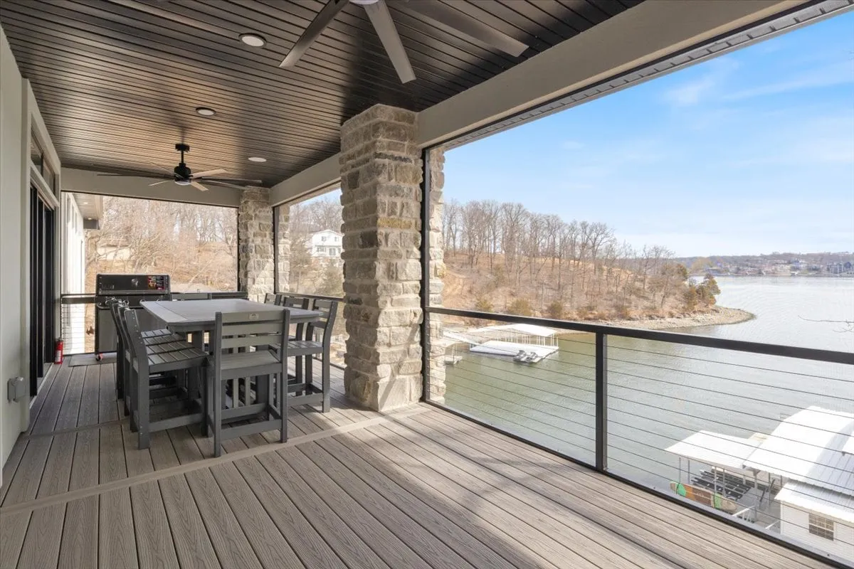 An elegant outdoor dining table on a deck, overlooking the lake and surrounded by stone columns. The view captures the sense of communal outdoor living with a backdrop of natural beauty.