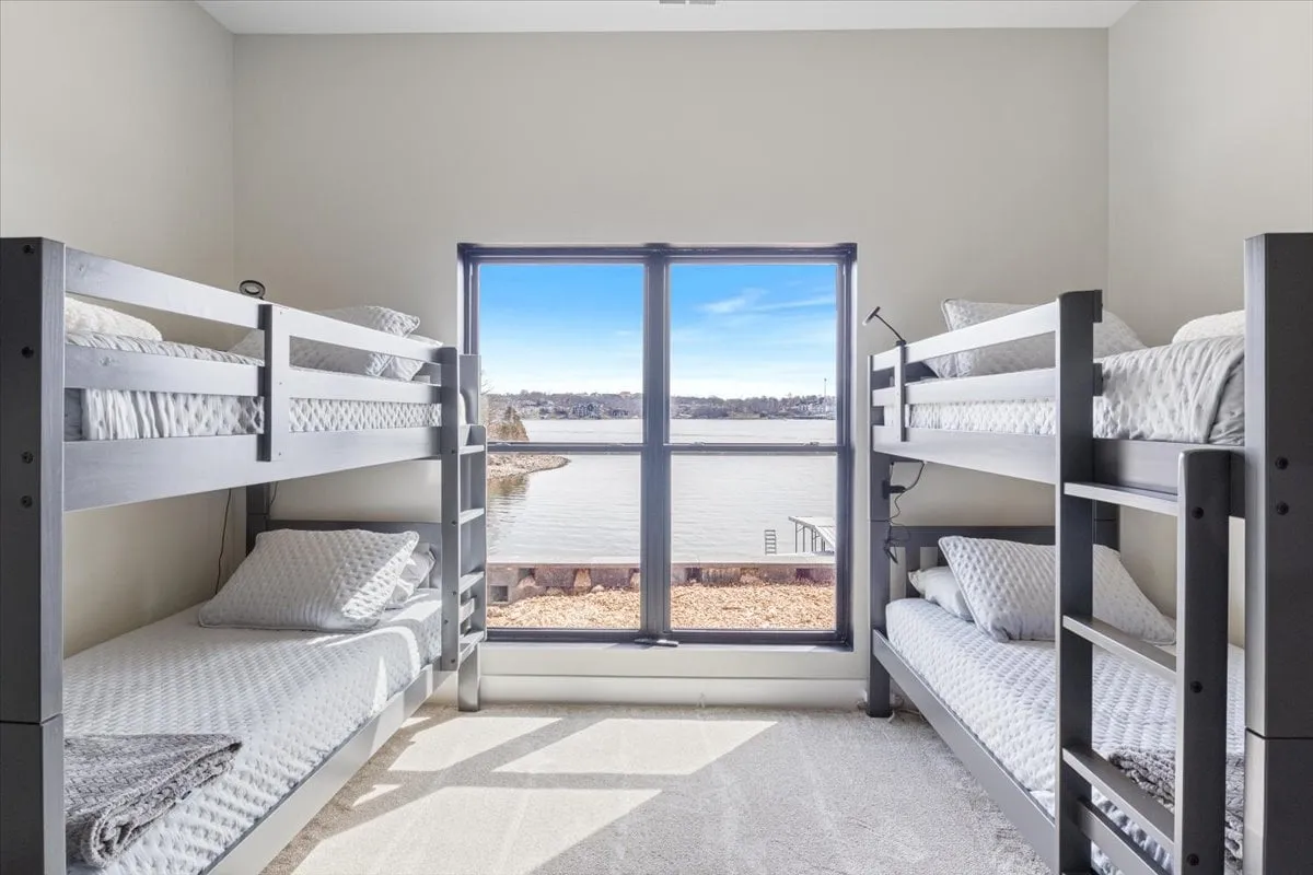 A cheerful bunk room with two bunk beds dressed in soft bedding, a large window offering a stunning view of the water, and an abundance of natural light. The space feels relaxed and comfortable, ideal for younger guests or families.