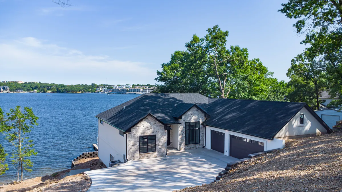 A striking exterior view with modern architecture nestled right on the waterfront, framed by a landscaped yard and serene lake backdrop. The scene suggests both luxurious relaxation and direct lake access.